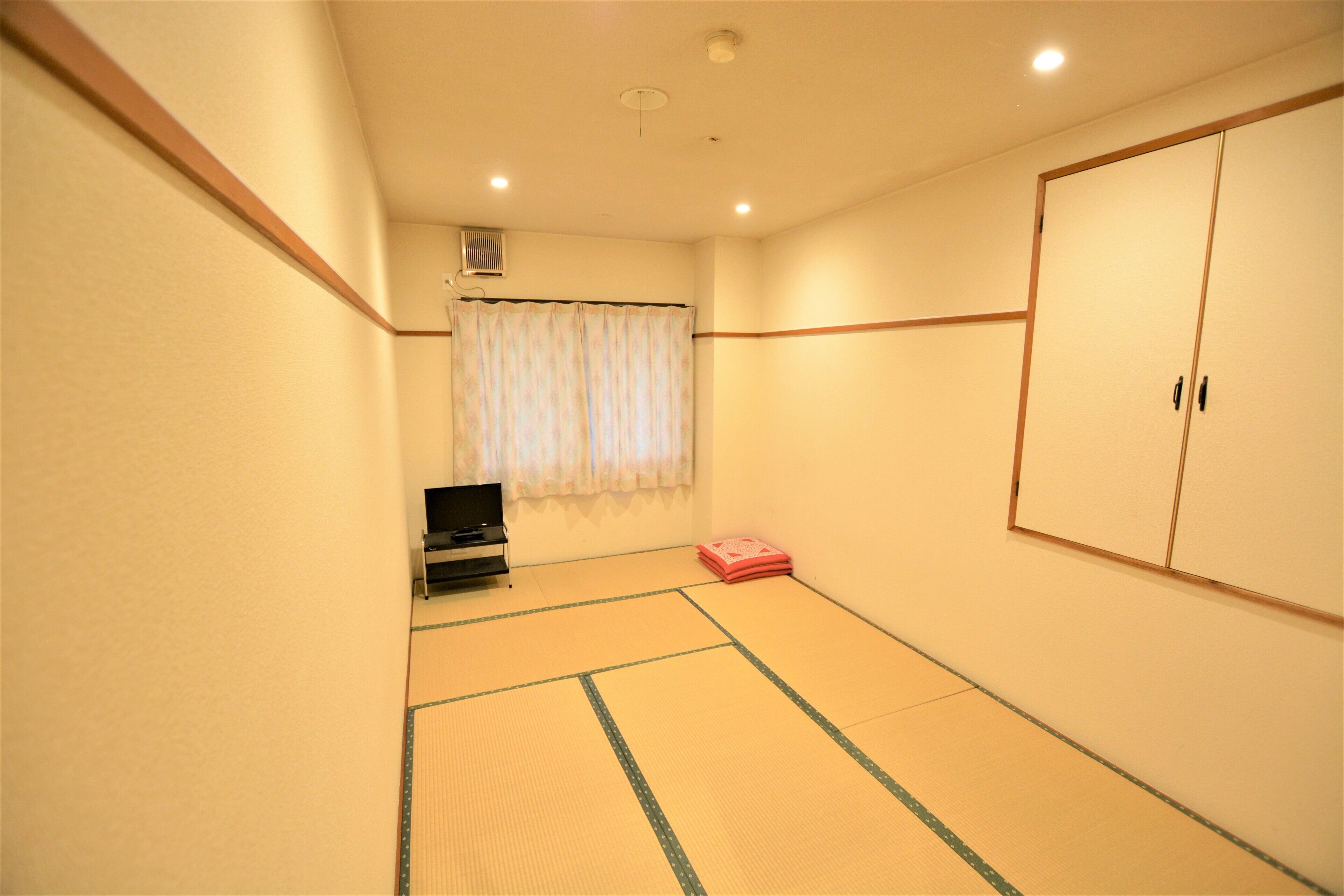 Una habitación con suelo de tatami, televisor, armario y ventana con cortina.