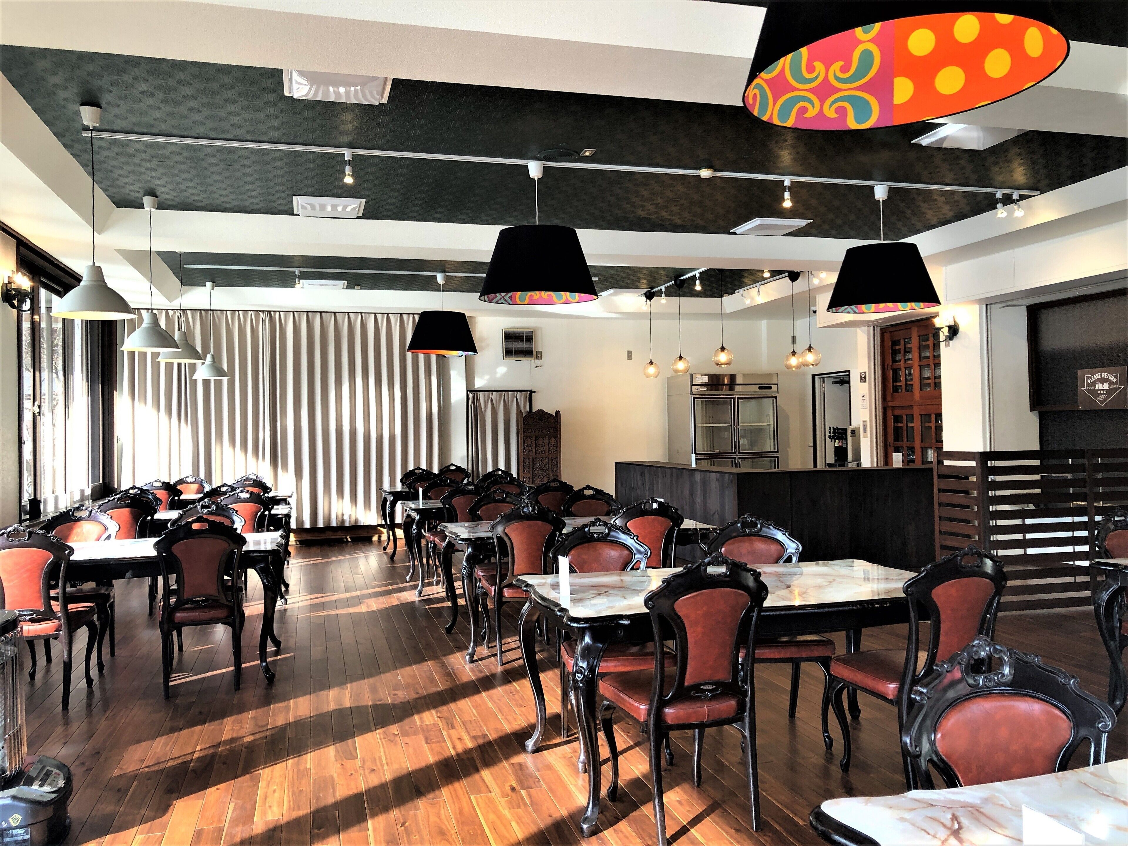 A restaurant with a long dining area, multiple tables, and chairs. There are hanging lights and a patterned ceiling.