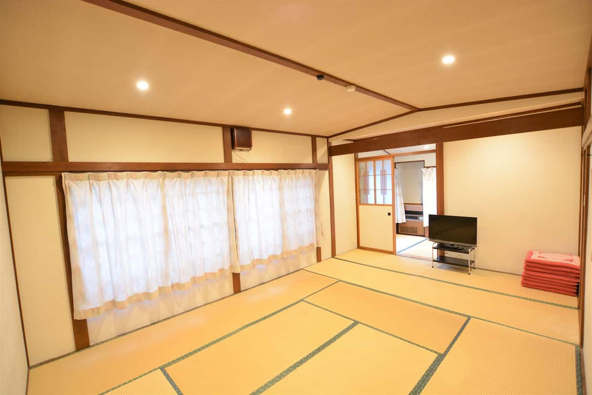 A traditional Japanese room with tatami flooring, a television, and a stack of red cushions.