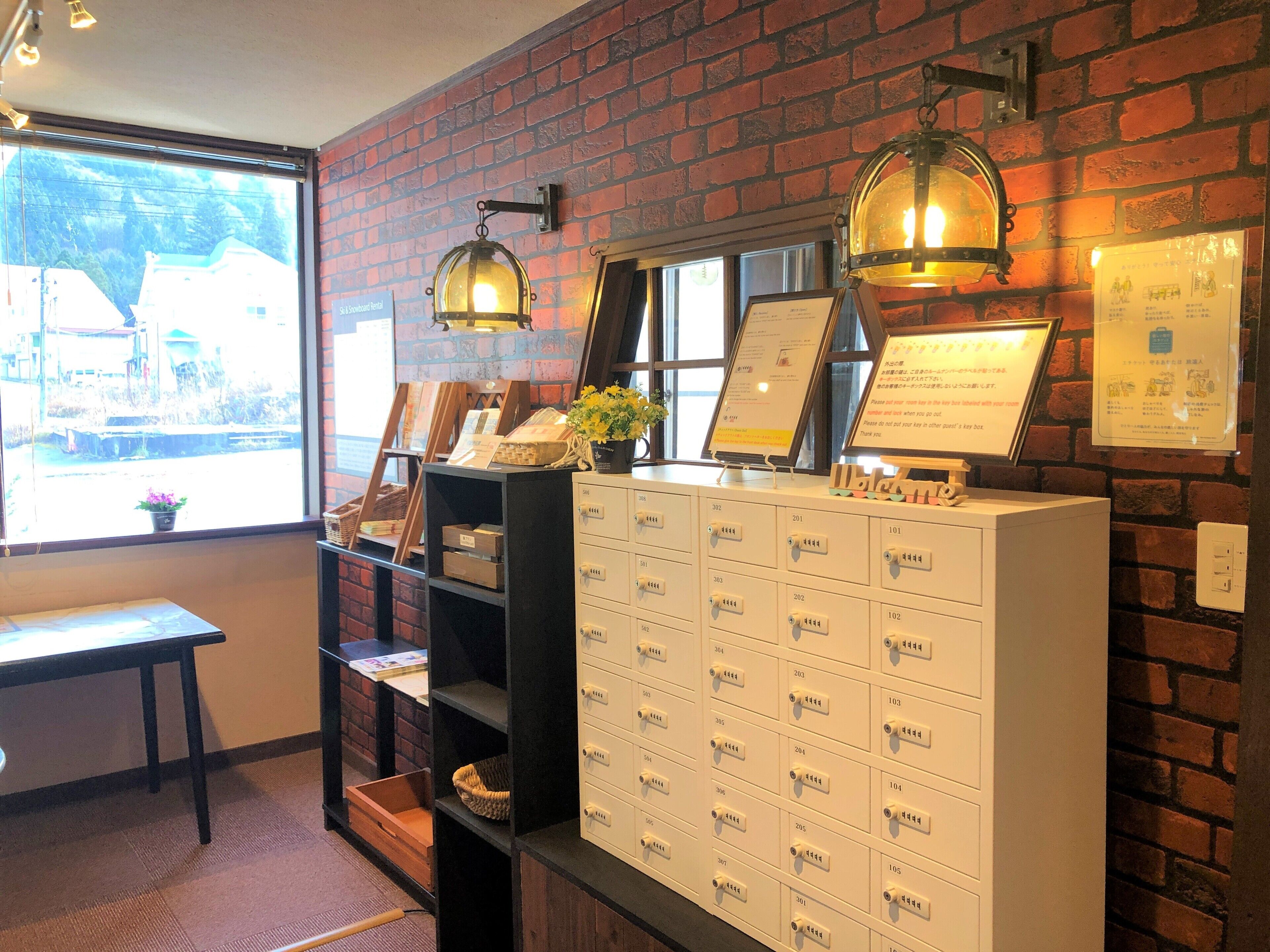 A reception area with a brick wall, a desk with a computer, a bulletin board, and a large white filing cabinet with drawers labeled with numbers.