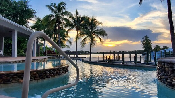 Une piscine bordée de pierres, des palmiers et une vue imprenable sur le coucher de soleil.