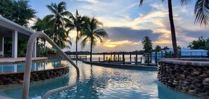 A swimming pool with a stone border, palm trees, and a sunset view. - Bay of Grace -- A Boater's Paradise Fantastic Sunsets Close to I-75 (Fort Myers)