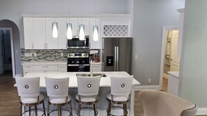 Une cuisine moderne avec des armoires blanches, des appareils en acier inoxydable et des luminaires suspendus.