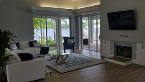 Un salon spacieux doté d’une cheminée, d’un téléviseur fixé au mur et de grandes fenêtres offrant une vue sur l’extérieur.