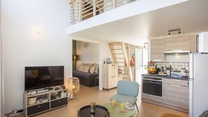 Un espacio habitable compacto con televisor, zona de estar, kitchenette y una escalera a un nivel superior.
