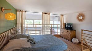 Un dormitorio con cama, cómoda, televisor y balcón con cortinas.
