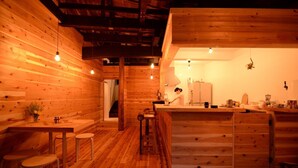 A cozy wooden cabin interior with a kitchen area, wooden walls, and a dining table with stools. - Hakone Guesthouse toi - Hostel (Hakone)