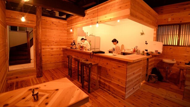 A wooden cabin interior with a kitchen area, bar stools, and a dining table. - Hakone Guesthouse toi - Hostel (Hakone)