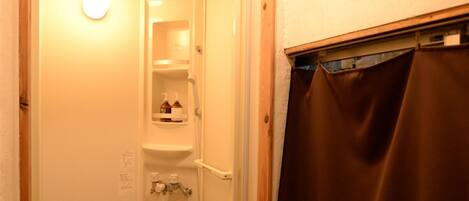 Un petit espace douche fermé, doté d’une porte, d’un porte-serviettes et d’une étagère pour les articles de toilette.