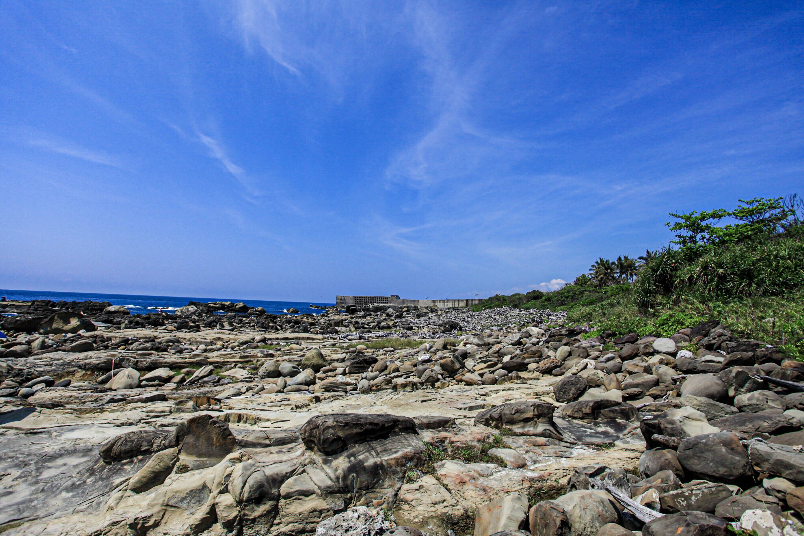 A rocky beach with large boulders and a clear blue sky.