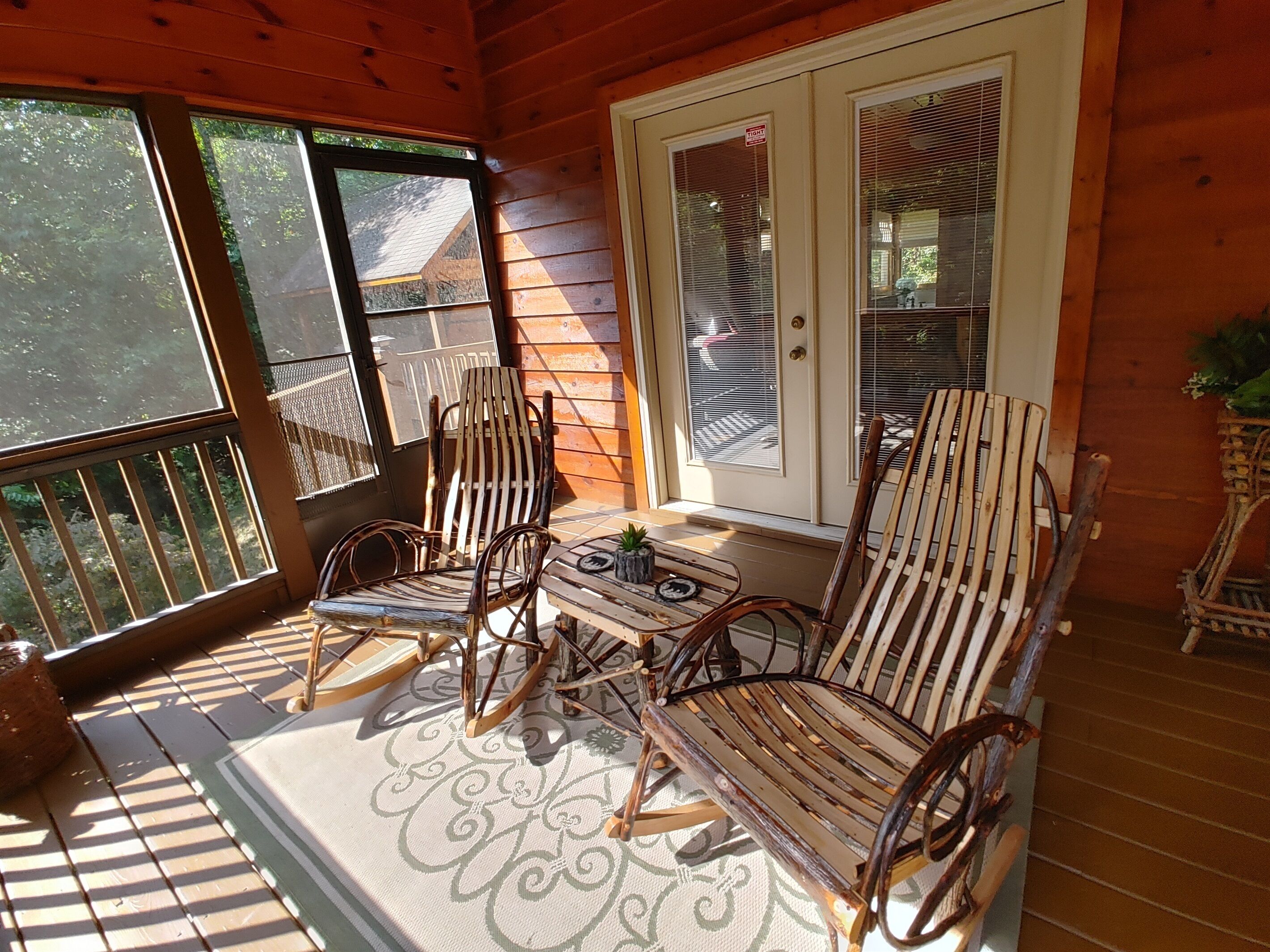 A wooden porch with two rocking chairs and a small table, a door with a 'TIGHT' sign, and a view of greenery outside.