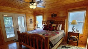 Ein gemütliches Schlafzimmer in einer Holzhütte mit einem Bett, einem Nachttisch, einer Lampe und einem Fenster mit Blick.