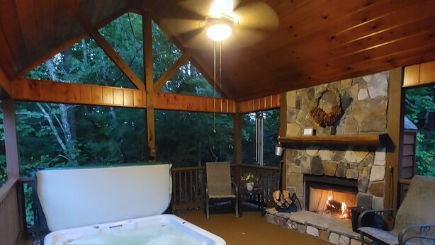 Eine Holzterrasse mit Whirlpool, Kamin aus Stein und Sitzgelegenheit im Freien.