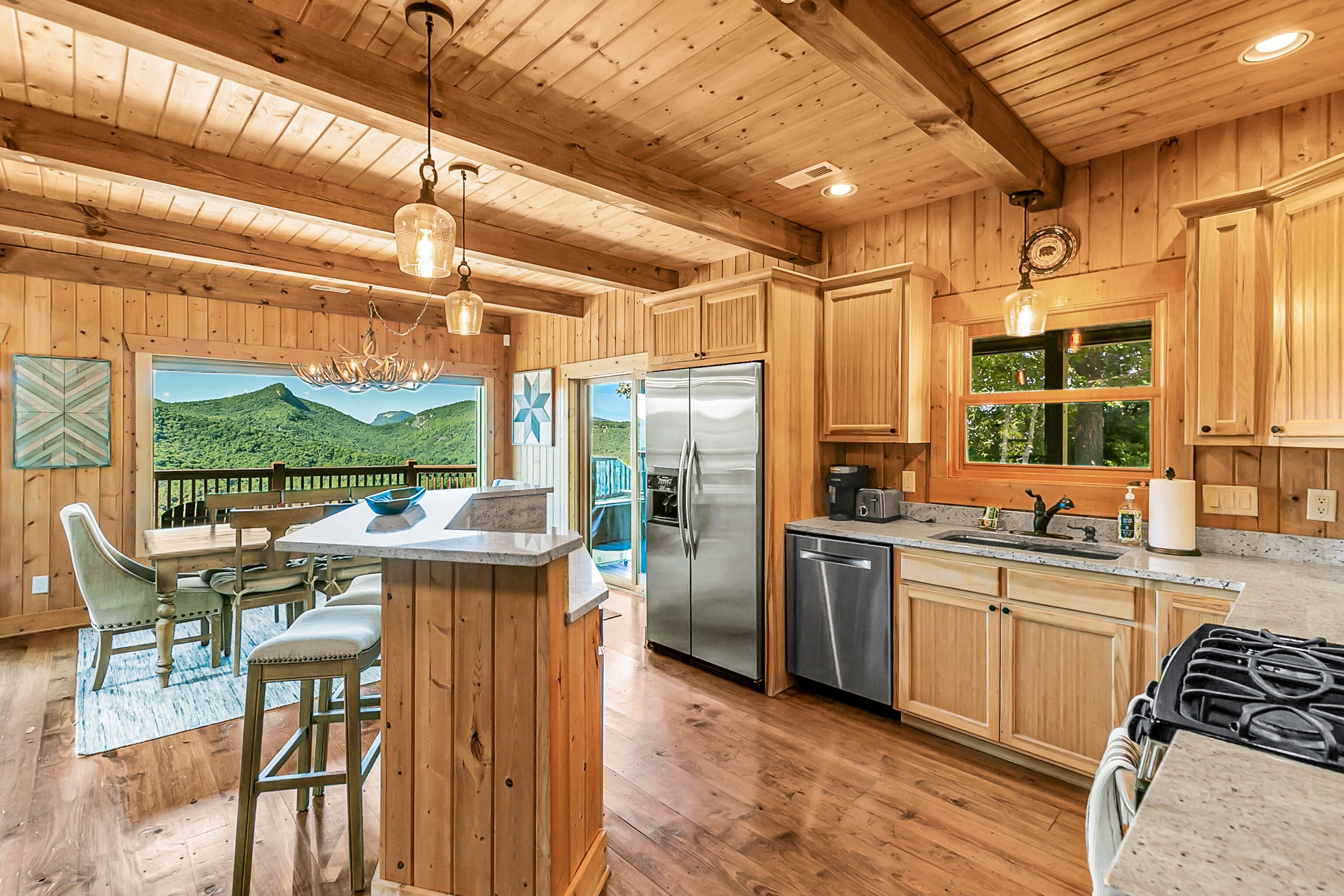 Une cuisine rustique aménagée dans une cabane en bois, avec un grand îlot central, des appareils en acier inoxydable et une vue sur l’extérieur.