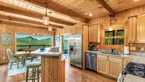 A wooden cabin kitchen with a large island, stainless steel appliances, and a view of the outdoors. - Magnificent Mountain Views (Sapphire)