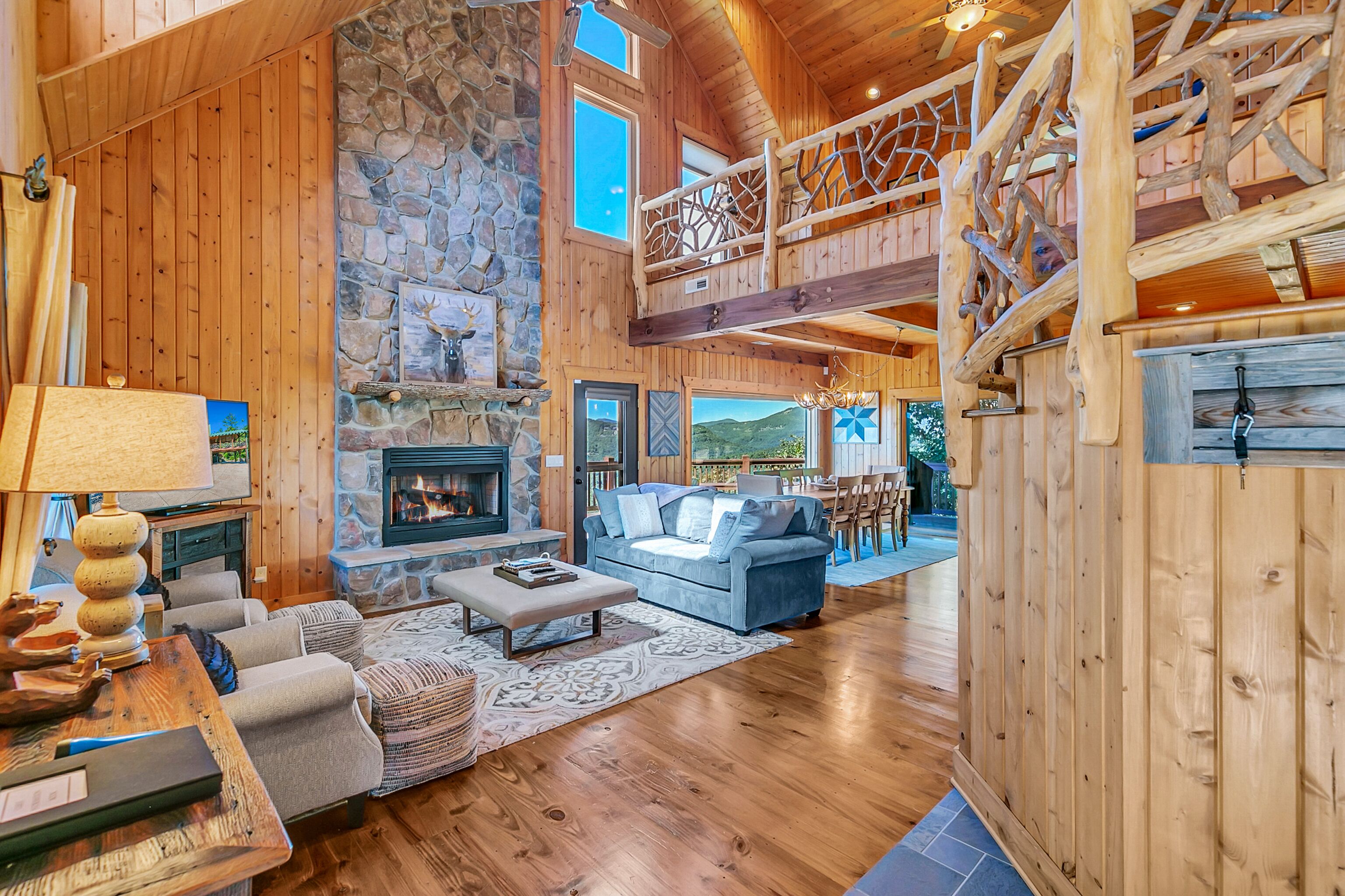 A spacious living room with a stone fireplace, a blue sofa, and a wooden staircase.