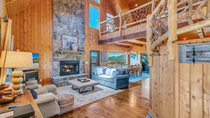 A spacious living room with a stone fireplace, a blue sofa, and a wooden staircase. - Magnificent Mountain Views (Sapphire)