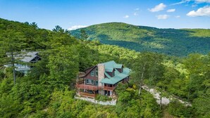 A large, multi-story wooden cabin with a green roof, surrounded by dense forest and hills. - Magnificent Mountain Views (Sapphire)