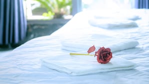 A bed with white linens and a single red rose.