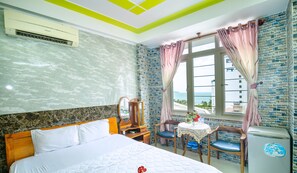 Ein Hotelzimmer mit Bett, Schreibtisch, Stuhl, Tisch mit Blumen, Kühlschrank und Fenster mit Vorhängen.