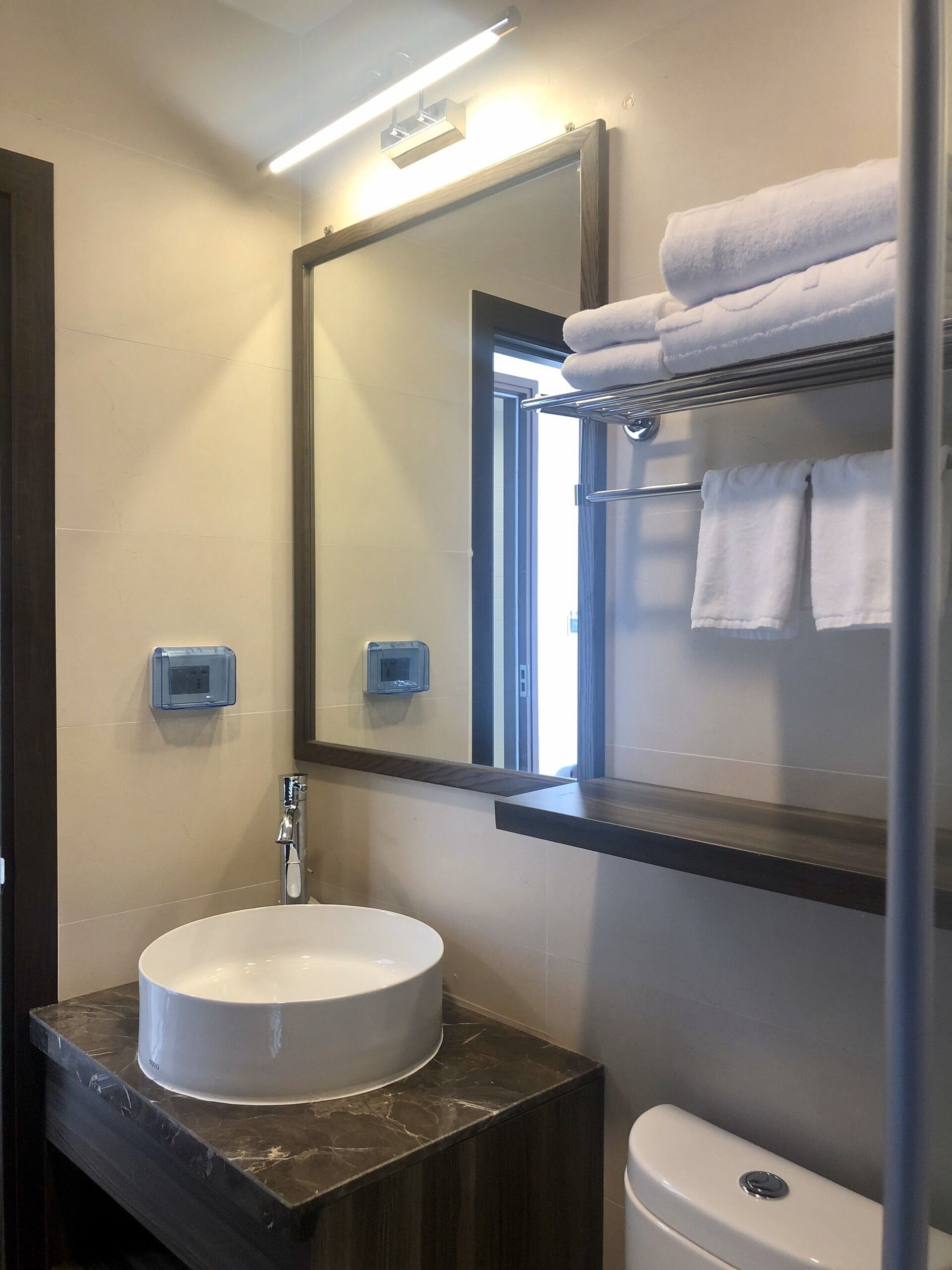A bathroom with a round sink, a mirror, a towel rack, and a toilet.