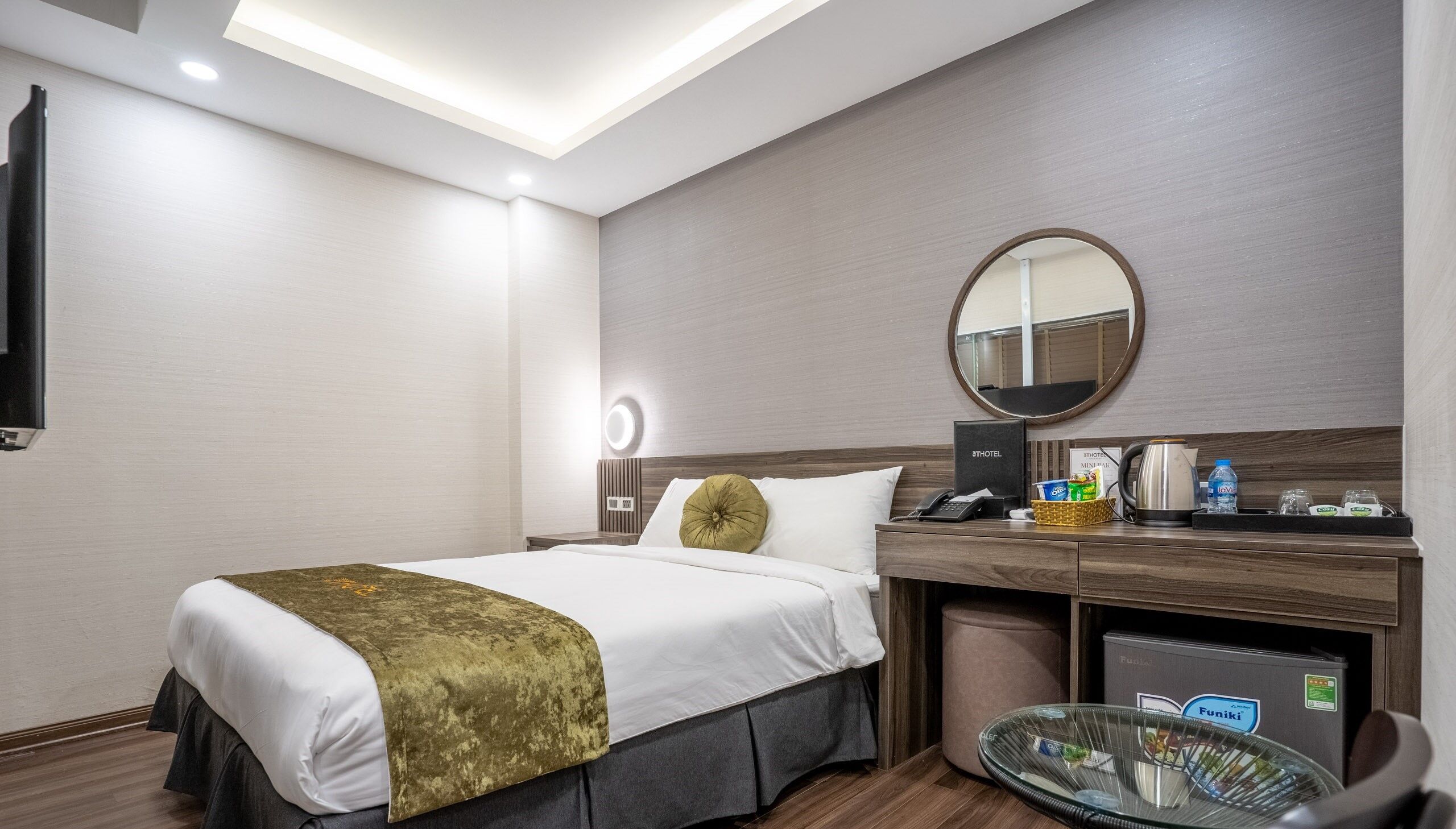 Ein Hotelzimmer mit Bett, Nachttisch, Spiegel und einem kleinen runden Tisch mit Glasplatte.