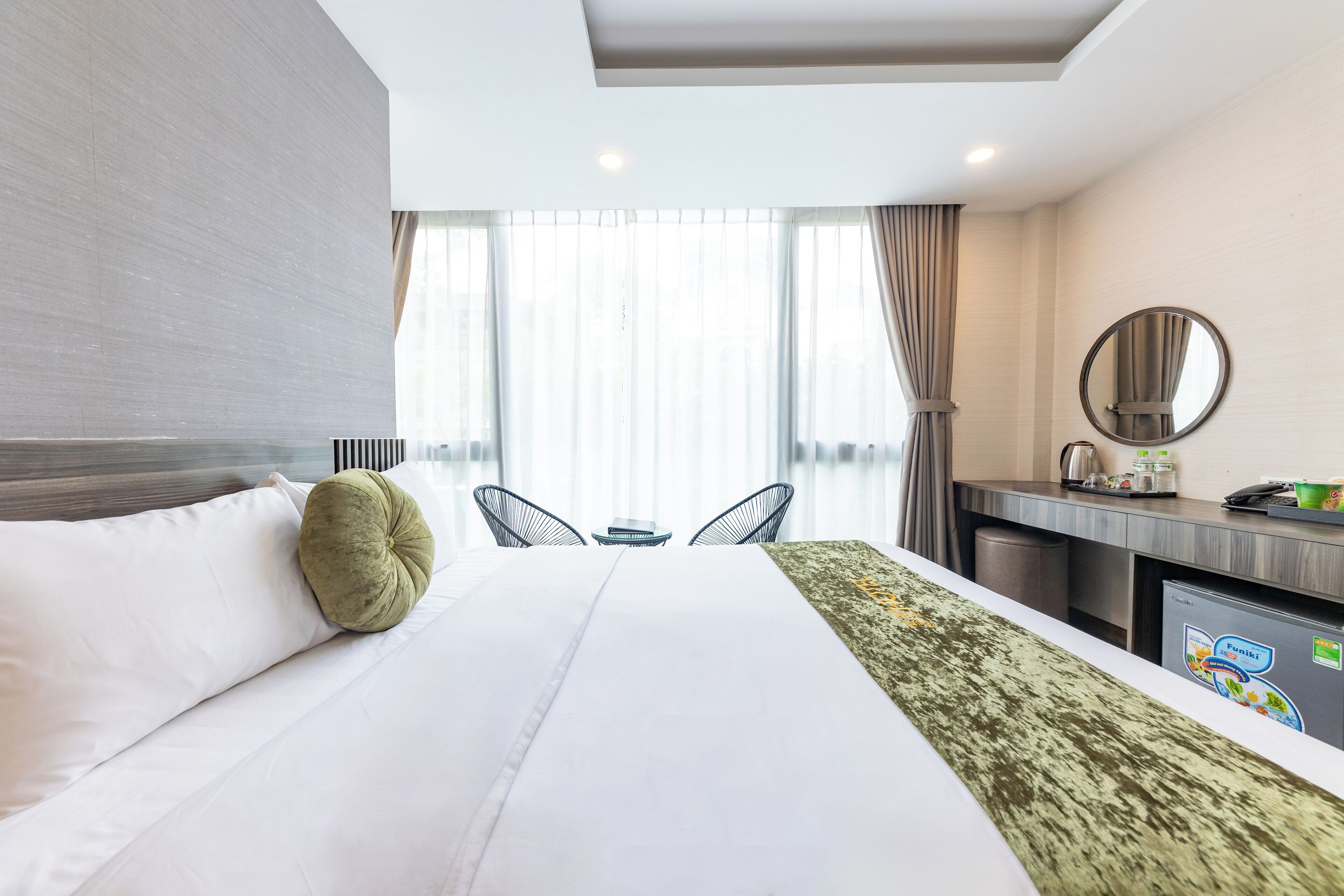 A hotel room with a bed, a desk, a chair, a mirror, and a window with curtains.