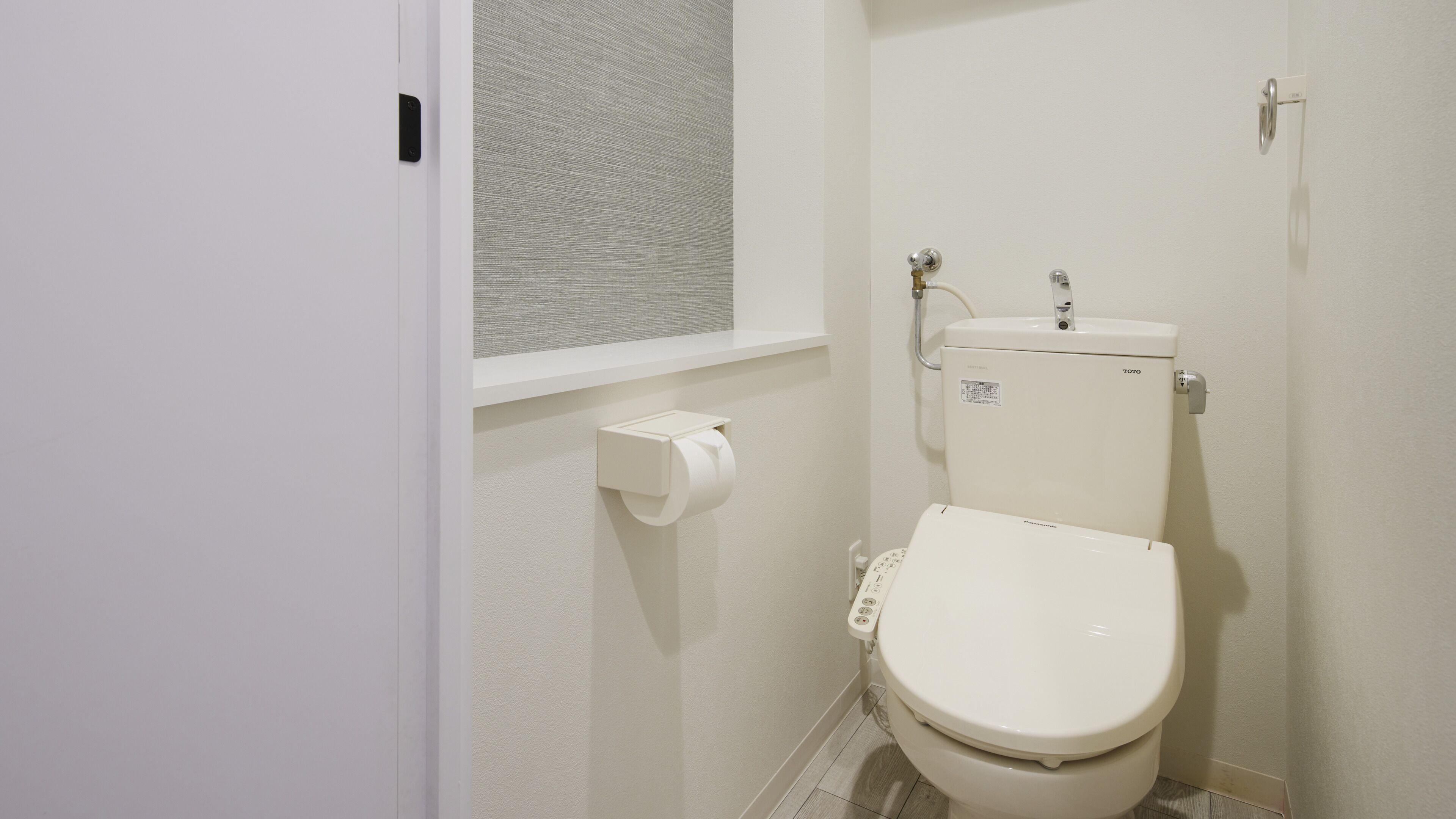 A small, clean bathroom with a toilet, a toilet paper holder, and a window with a textured view.