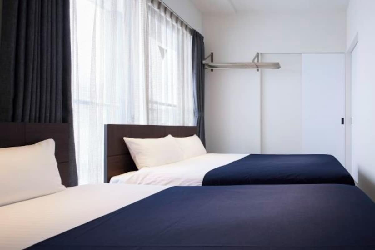 A hotel room with two beds, a headboard, a window with curtains, and a wardrobe.
