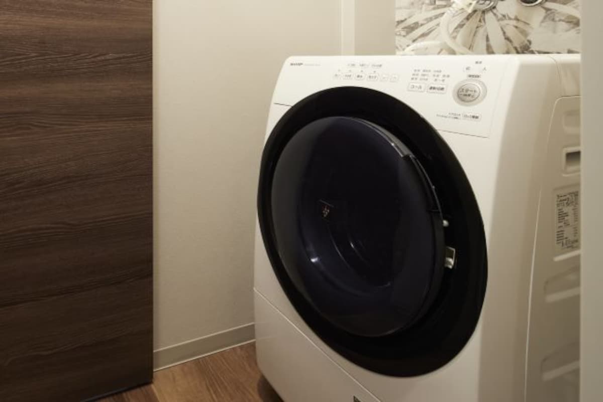 A front-loading washing machine in a room with a wooden floor and a white wall.