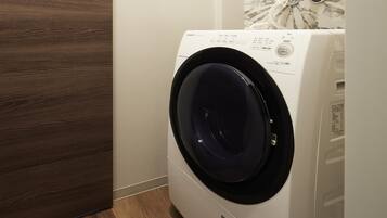 A front view of a white washing machine with a black door, located in a room with wooden flooring and a white wall.