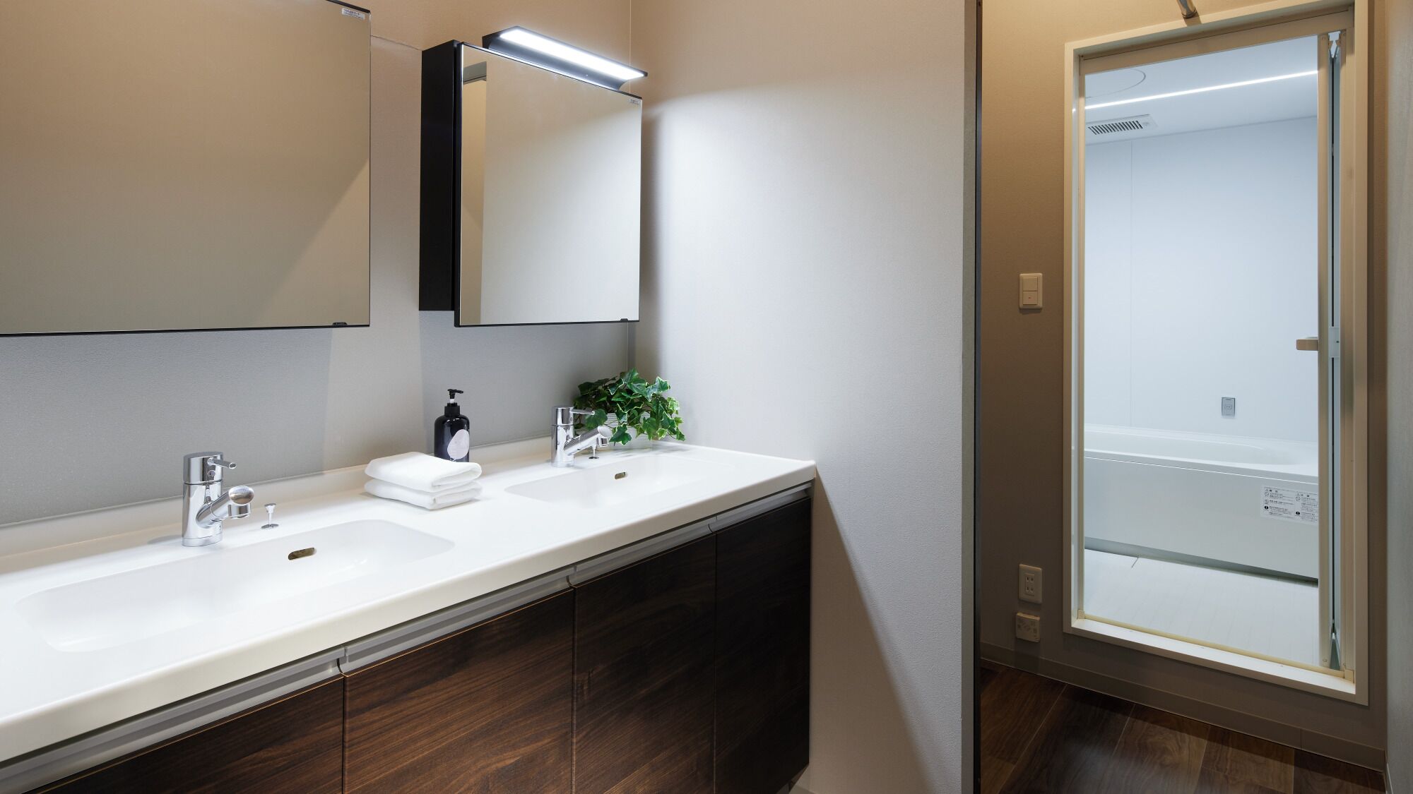 A modern bathroom with a large mirror, two sinks, a shower, and a dark wood vanity.