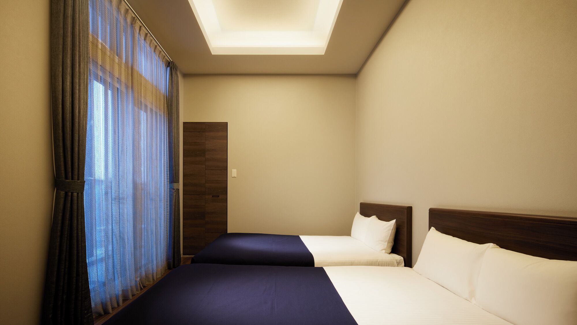 Habitación de hotel con dos camas, un tragaluz y un amplio ventanal con cortinas.