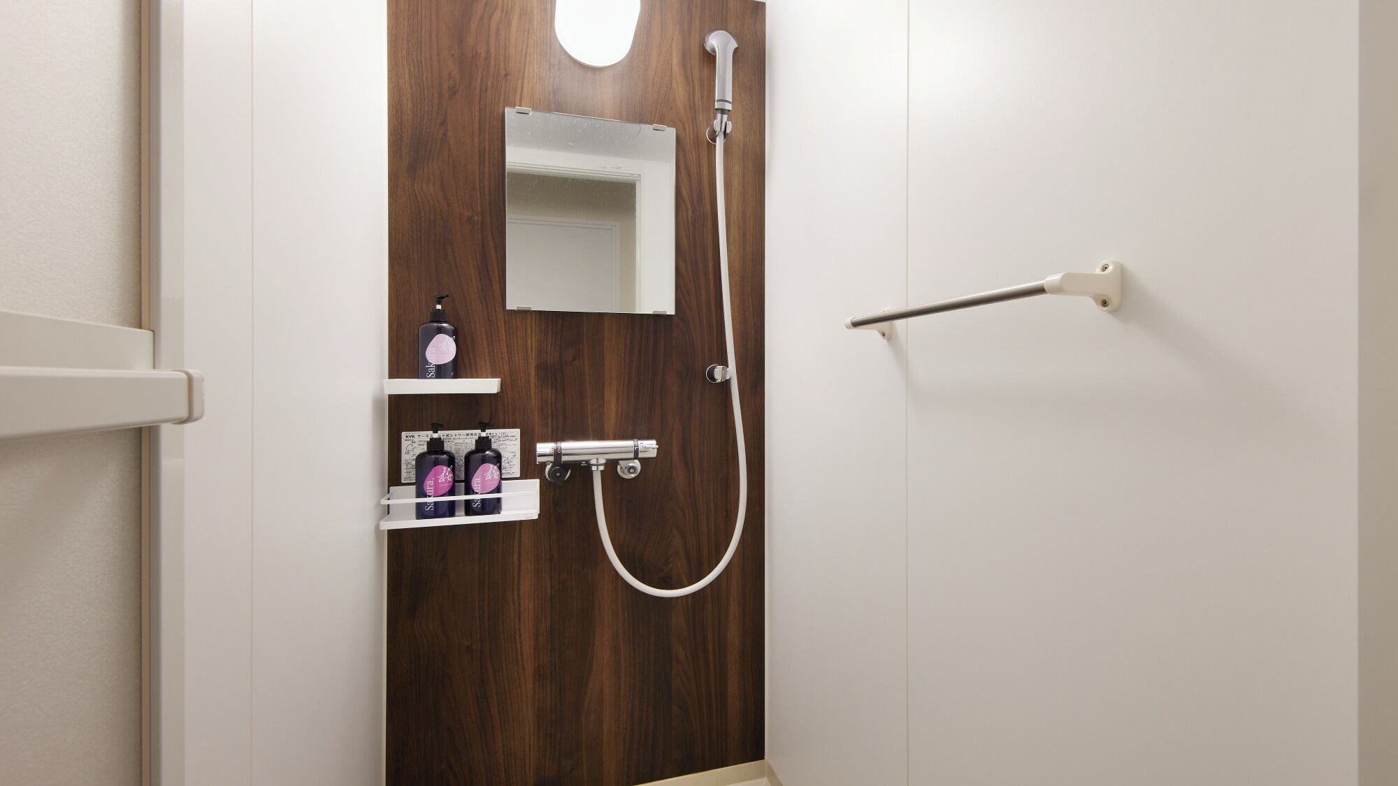 A bathroom with a wooden door, a white towel rack, a showerhead, and a shelf with toiletries.