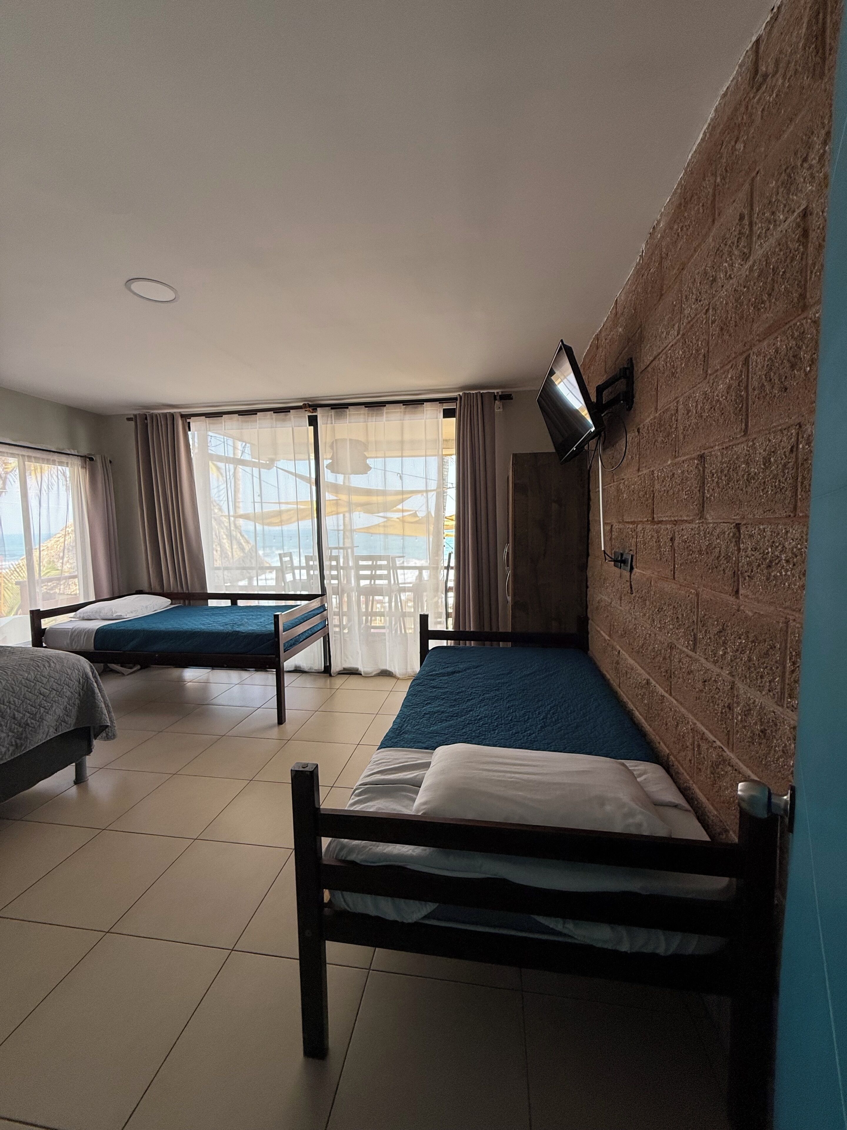 A room with two beds, a TV mounted on the wall, and a large window with curtains.