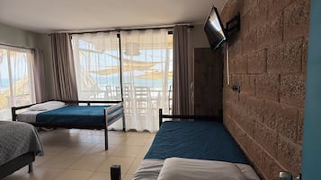 Una habitación con dos camas, un televisor montado en la pared y un ventanal con cortinas.