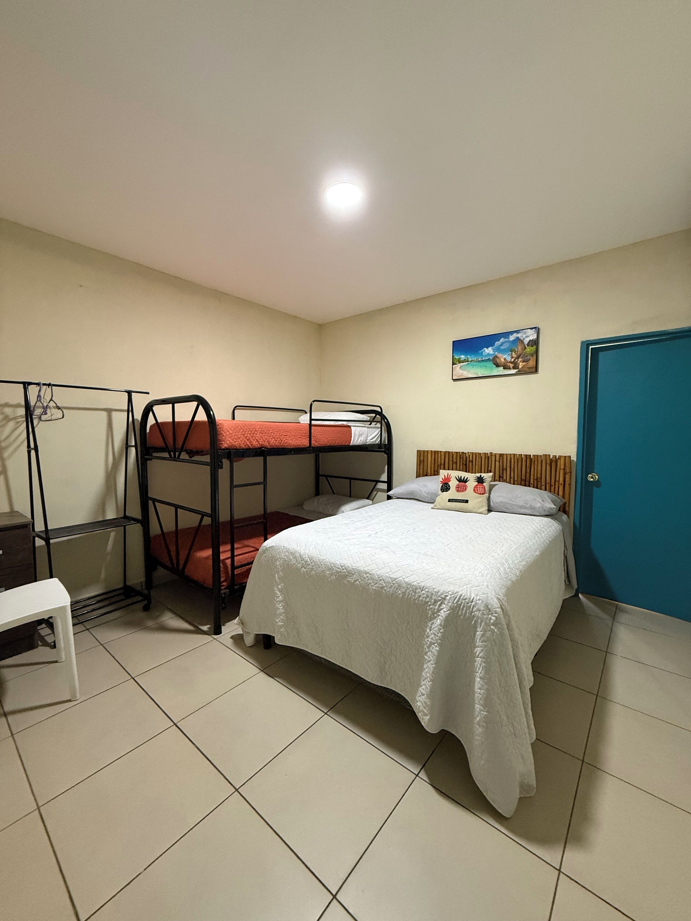 Een kamer met stapelbedden, een enkel bed, een deur, een aan de muur hangend schilderij en een betegelde vloer.