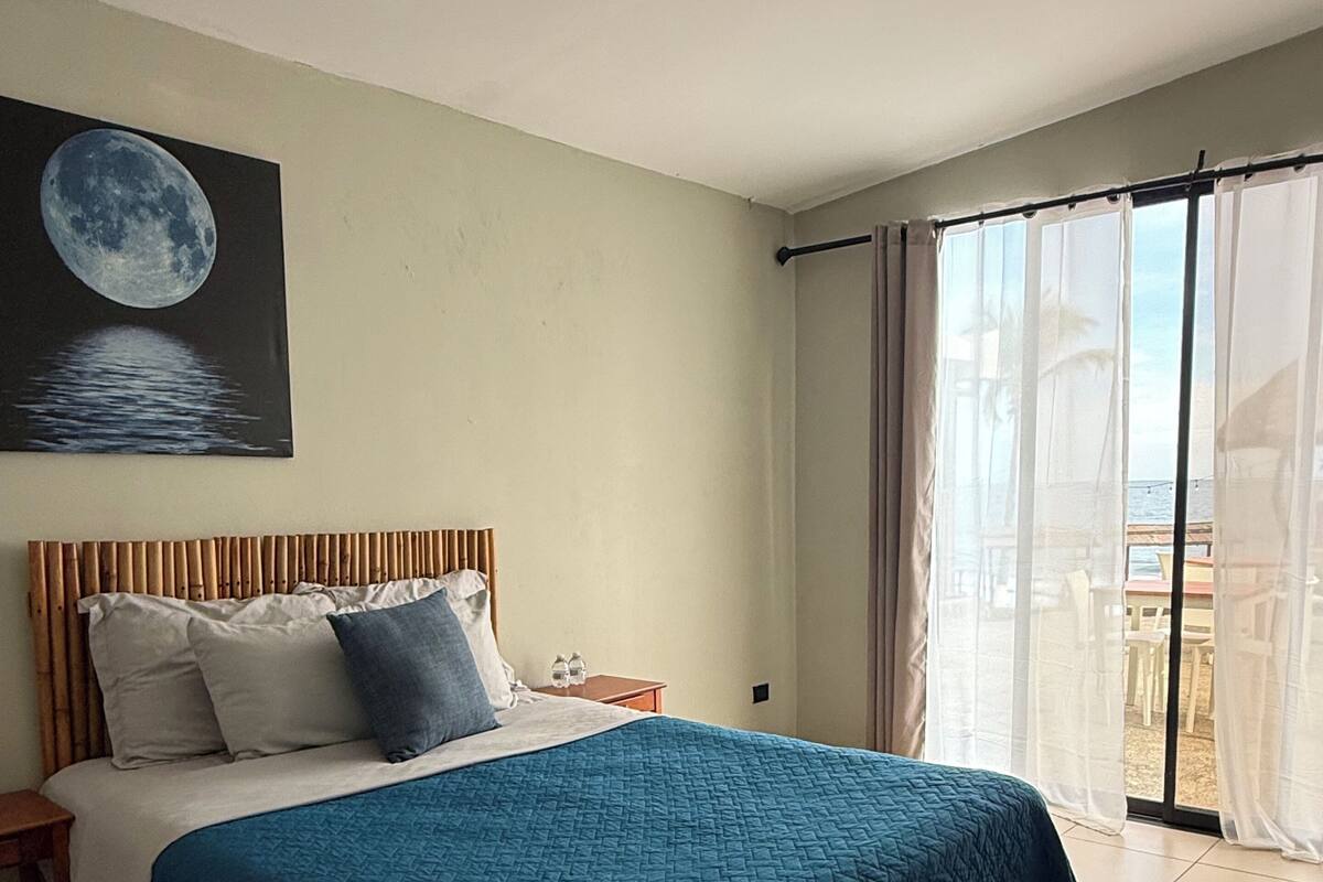 A hotel room with a bed, a nightstand, a window with curtains, and a moon painting on the wall.