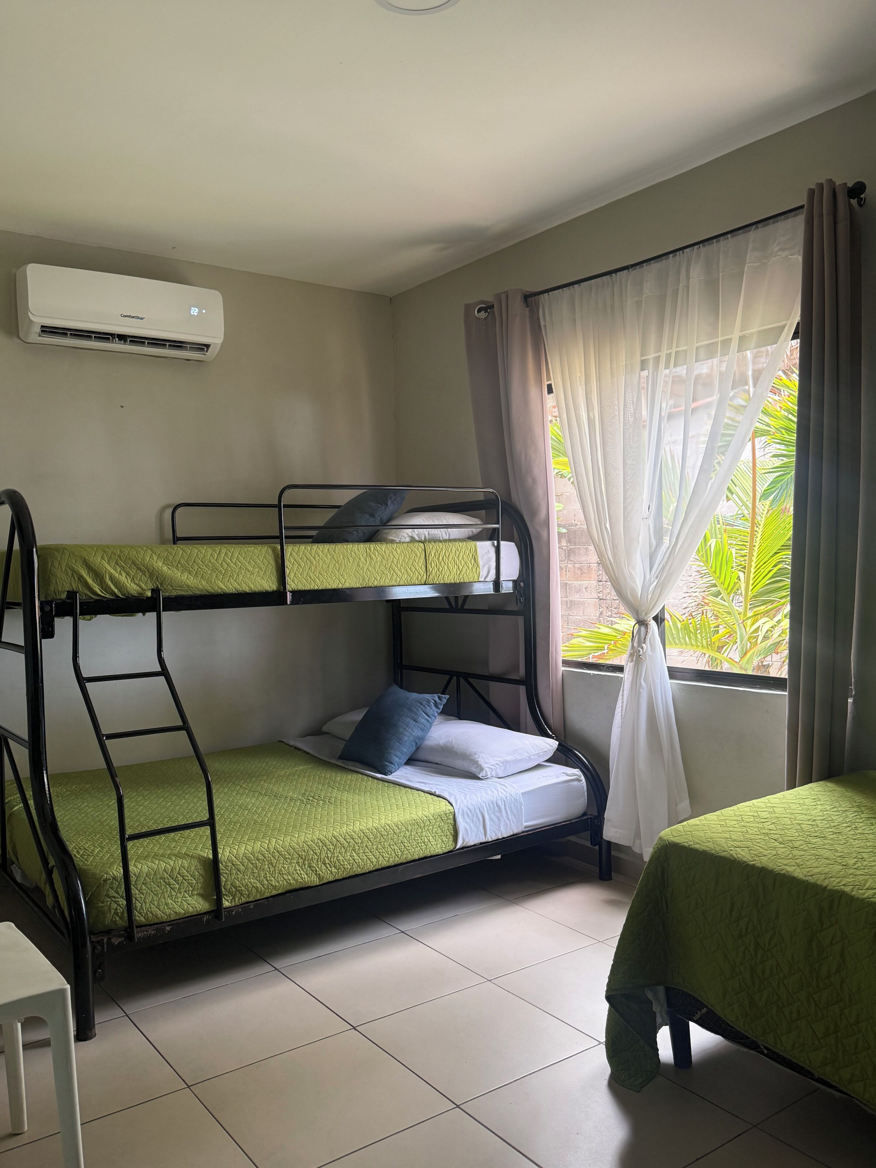 Une chambre avec des lits superposés, une fenêtre avec des rideaux, un radiateur et une petite table.