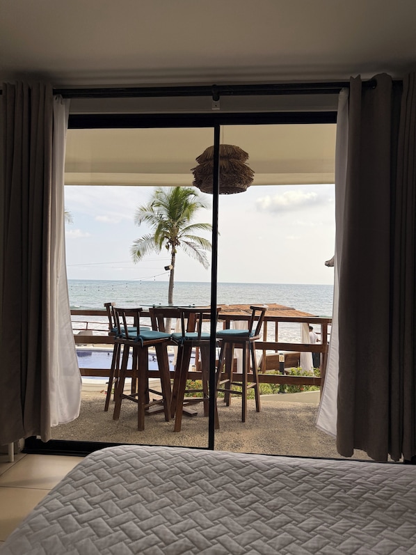 Een kamer met een bed, uitzicht op de oceaan, een palmboom en een tafel met stoelen.