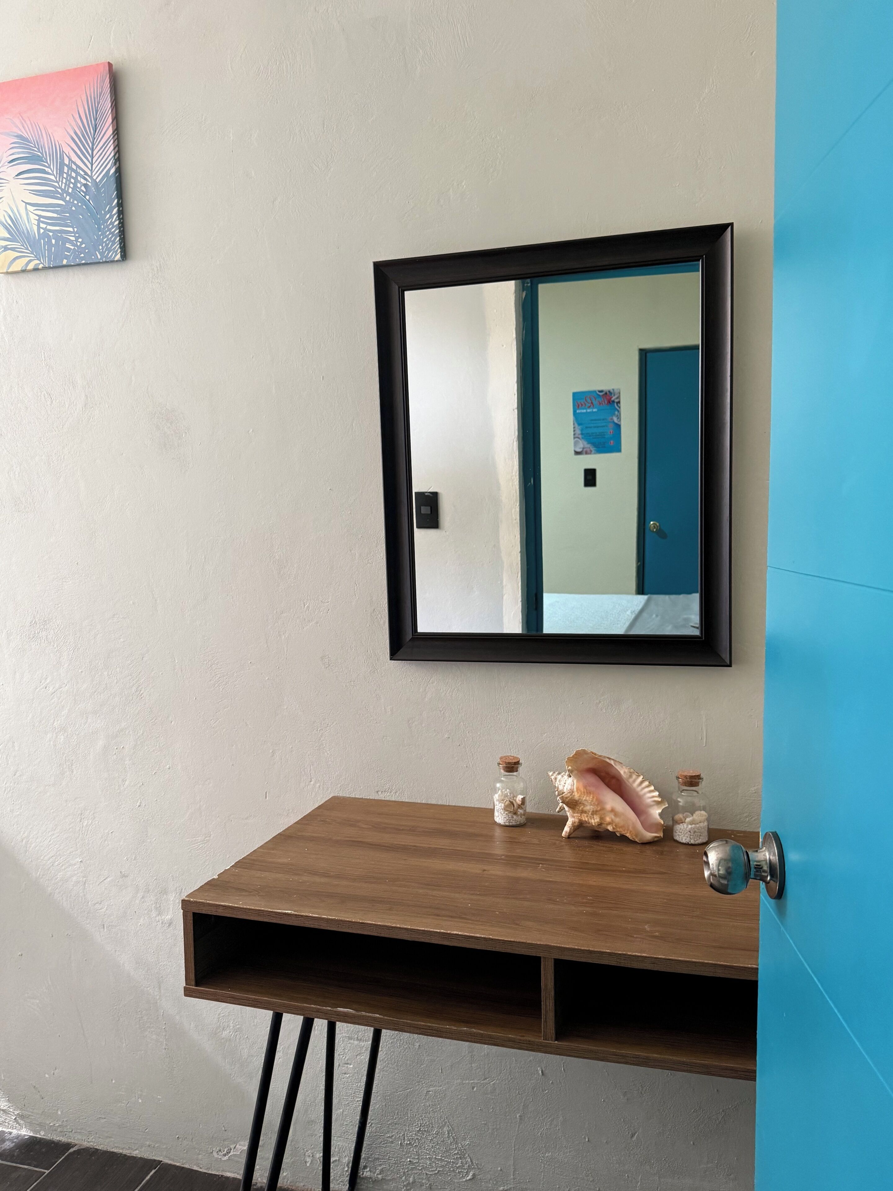 A bathroom with a wooden vanity, a mirror, a blue door, and a small shelf with decorative items.