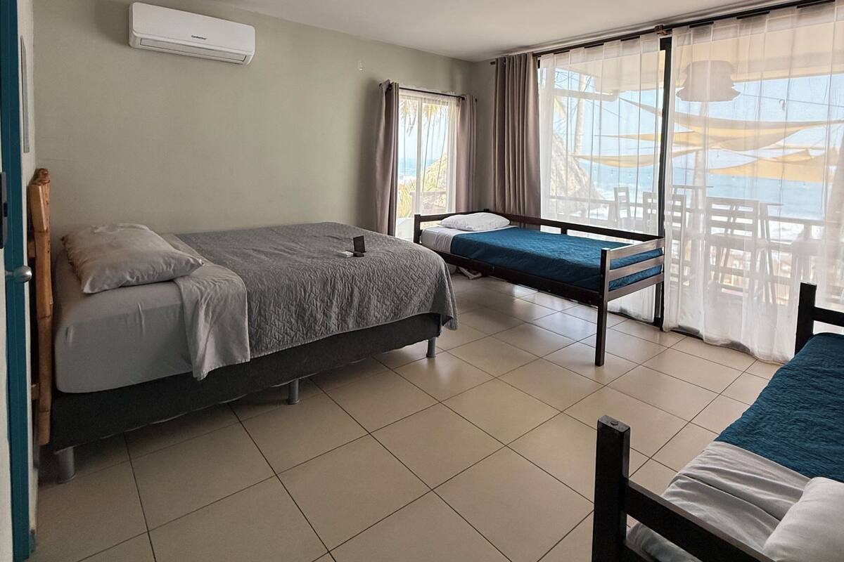 A room with two beds, a window with curtains, a ceiling fan, and a view of the outdoors.