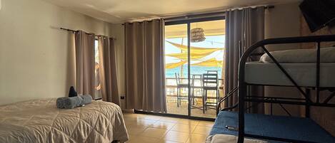 Quarto de hotel com duas camas, varanda com mesa e cadeiras, e vista para a praia.