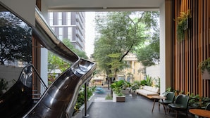 A modern indoor space with a metallic slide, seating area, and potted plants. - MEANDER Saigon (Ho Chi Minh City)