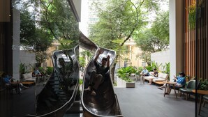 A modern indoor space with two metallic slides, seating areas, and potted plants. - MEANDER Saigon (Ho Chi Minh City)