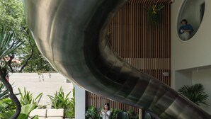 A modern indoor space with a curved metallic structure, seating areas, and indoor plants. - MEANDER Saigon (Ho Chi Minh City)