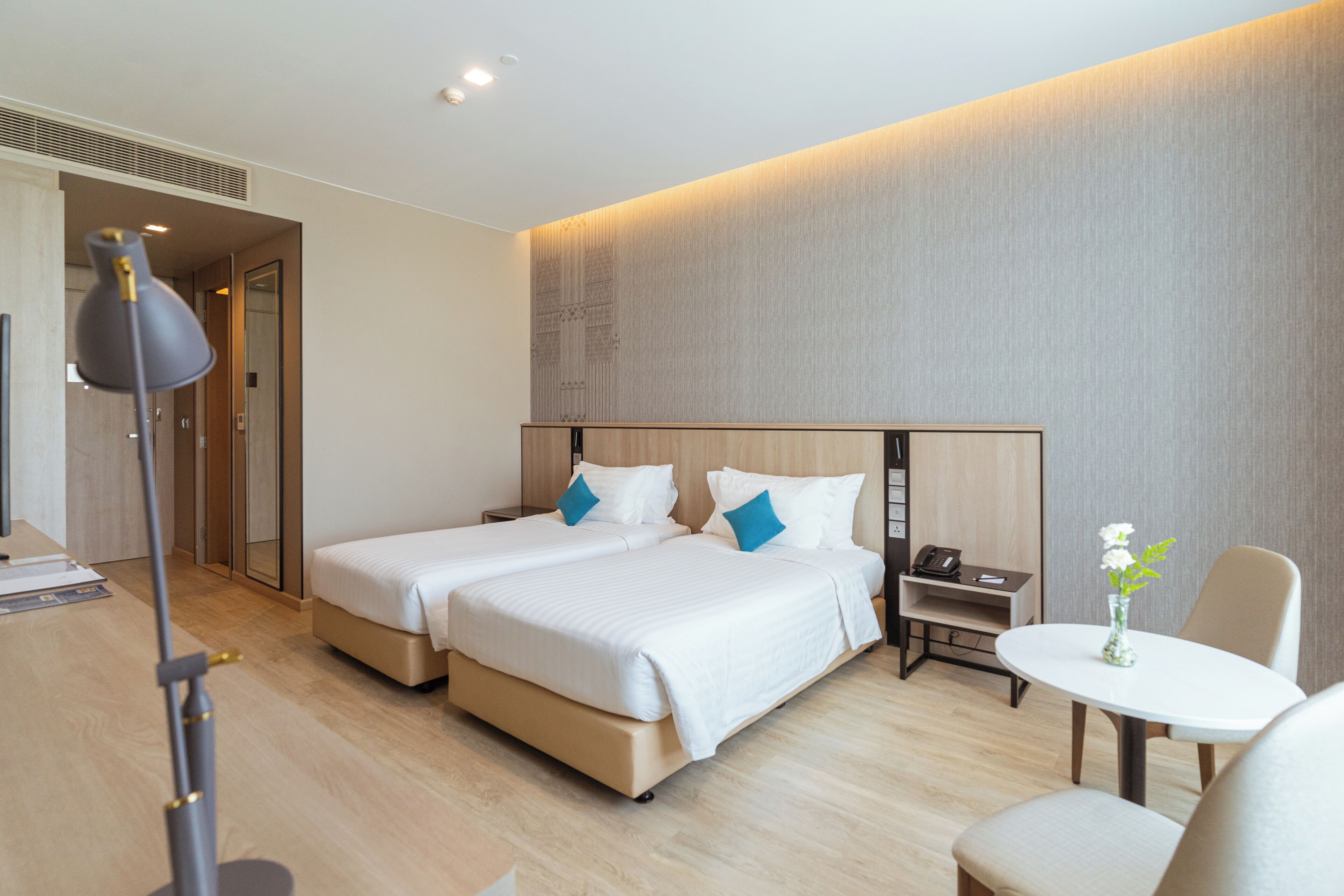 Une chambre d’hôtel avec deux lits, un bureau, une chaise, une petite table et un vase avec des fleurs.