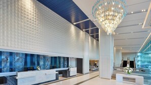 Eine moderne Hotelhalle mit einer Rezeption, einem großen Chandelier und einer Glasstiege.