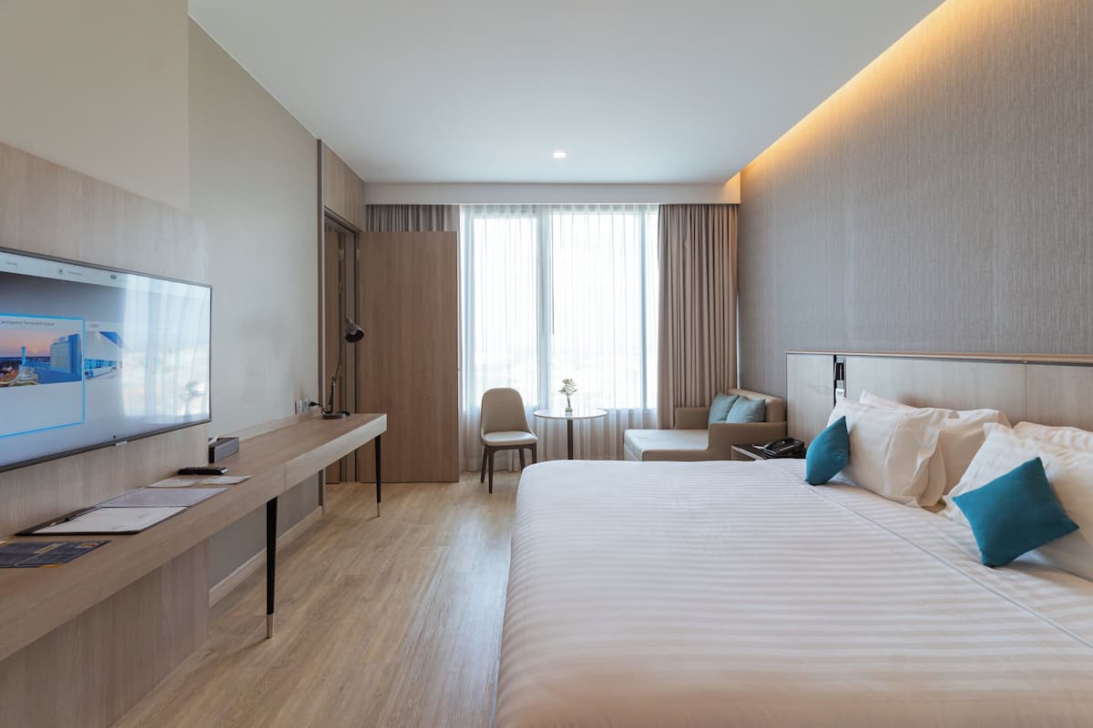 A hotel room with a large bed, a desk, a chair, a small table, and a TV.
