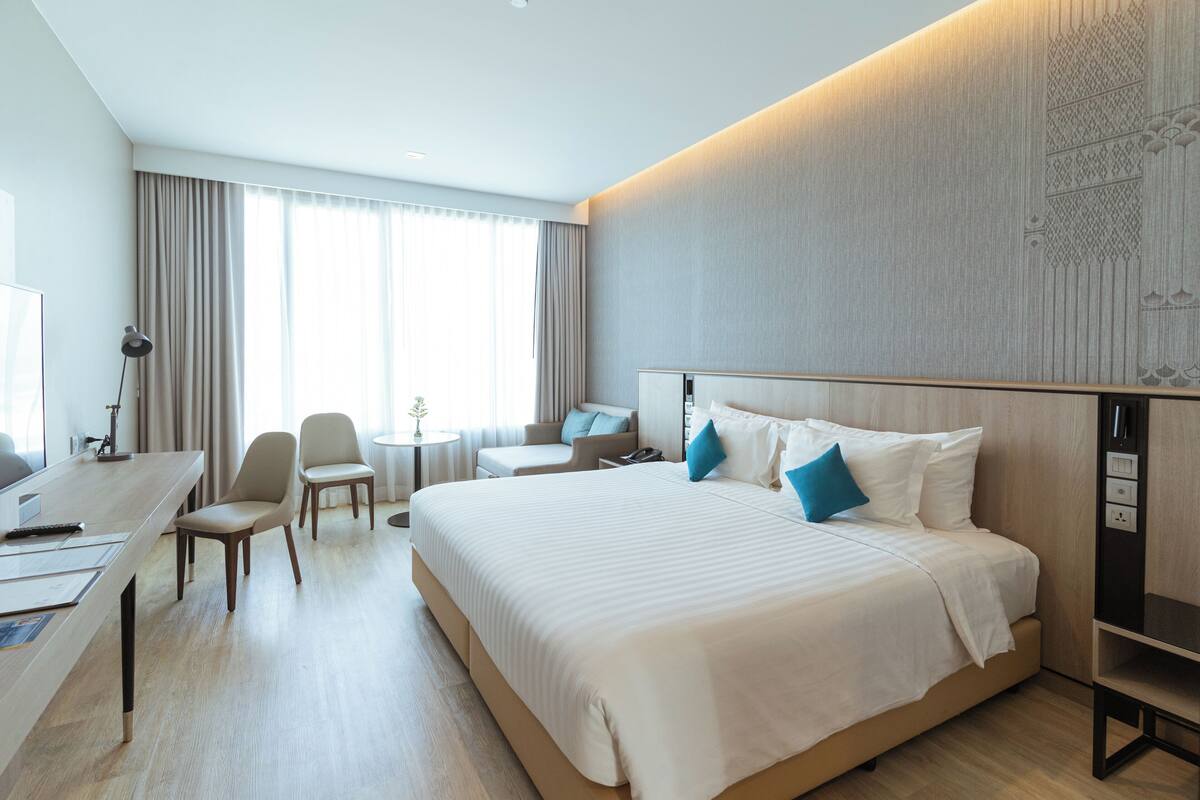 A modern hotel room with a large bed, a desk, and a seating area.